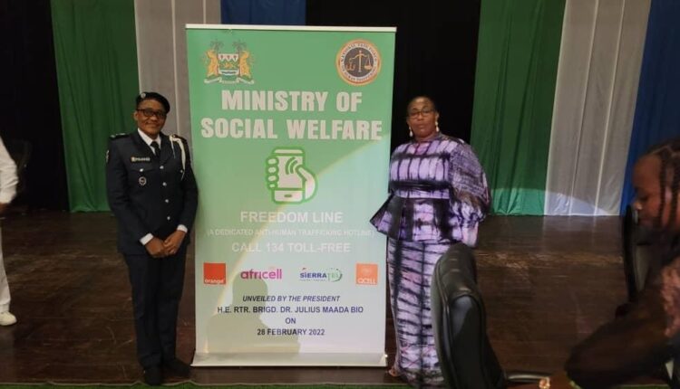 Madame Marie Gomez devant une affiche de la conférence internationale sur la traite des personnes